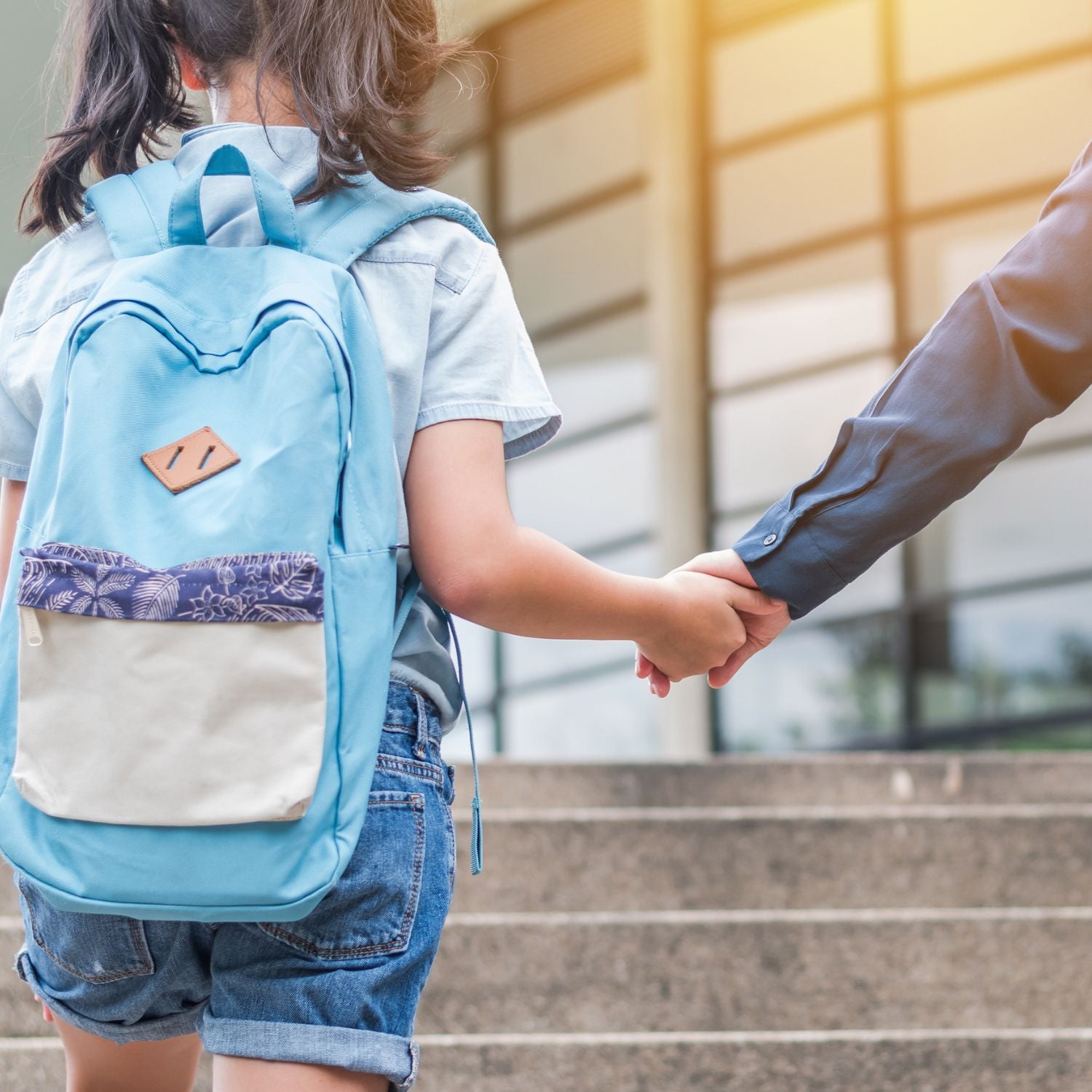 Back to school - girl wearing denim shorts, blue shirt and blue backpack going into school building