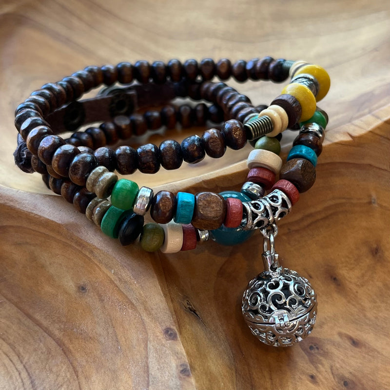 Essential oil wrap with dark wood beads and muted blue, green, and other earthy toned beads. Silver cage pendant holds a lava rock for essential oils.