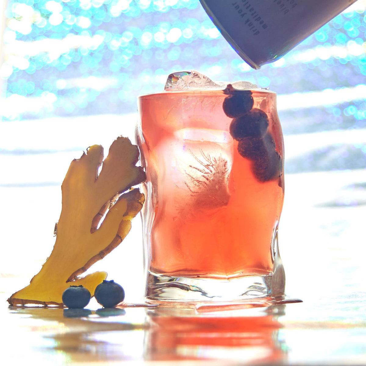 A glass of red blueberry and ginger botanical water with blueberries and ice in the drink