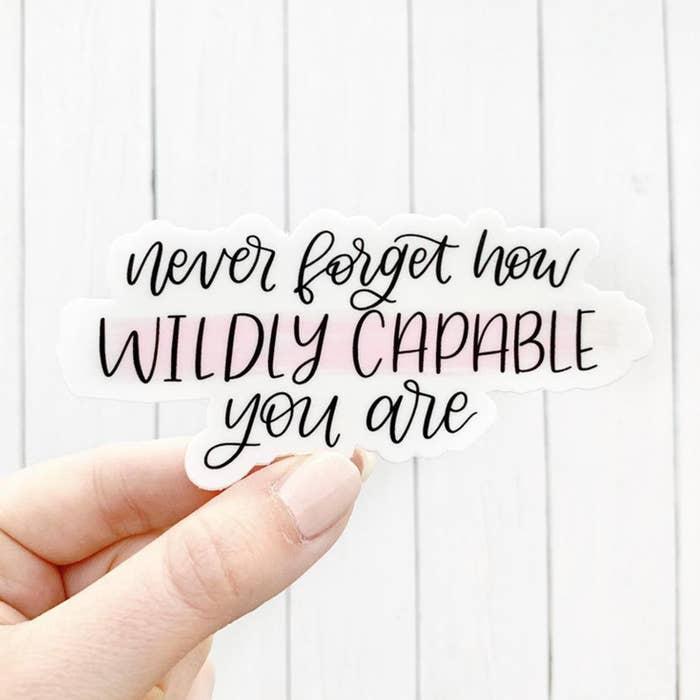 "Never forget how wildly capable you are" is printed in black on this white sticker with a faint blush pink background.