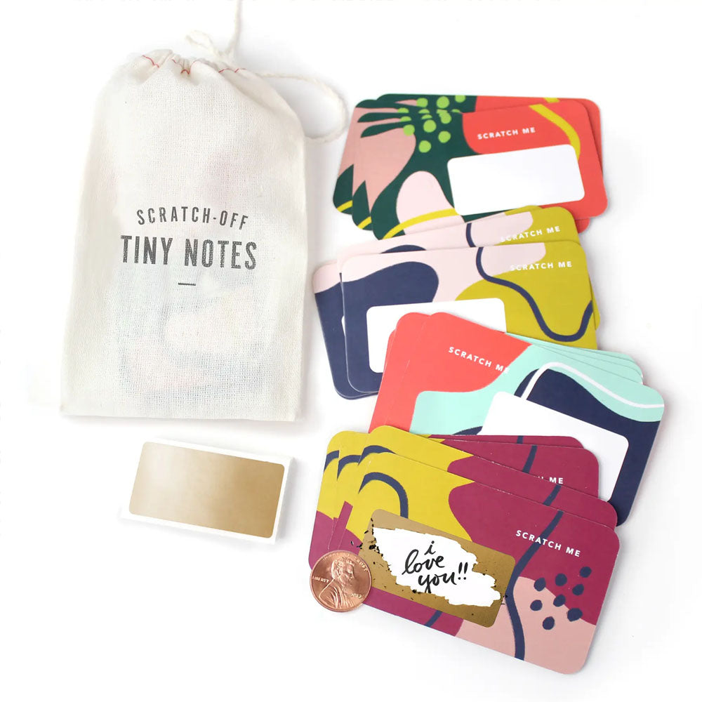 Cotton bag labeled "Scratch-off Tiny Notes", assorted scratch off cards to the side, and gold scratch off stickers