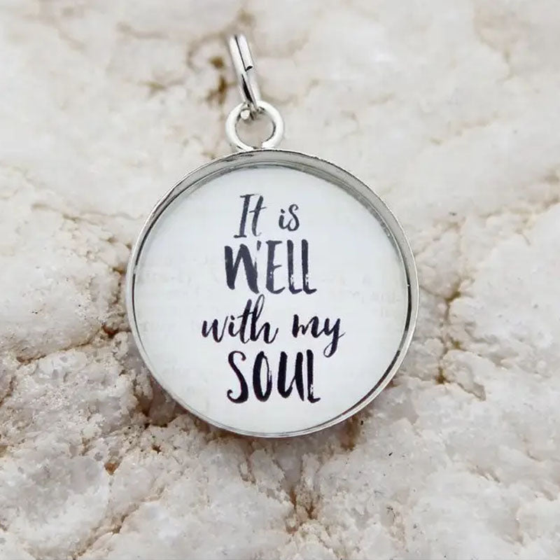 Round white necklace pendant with a silver metal edge that reads, "It is well with my soul"