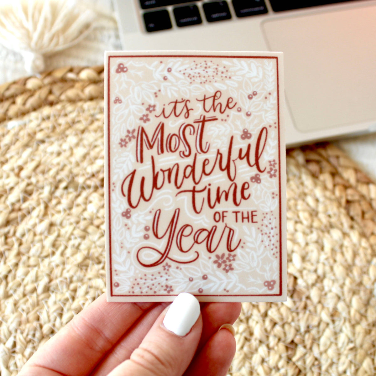 Peach colored sticker with a white and dark peach colored holly pattern in the background and "It's the most wonderful time of the year" written in dark peach color