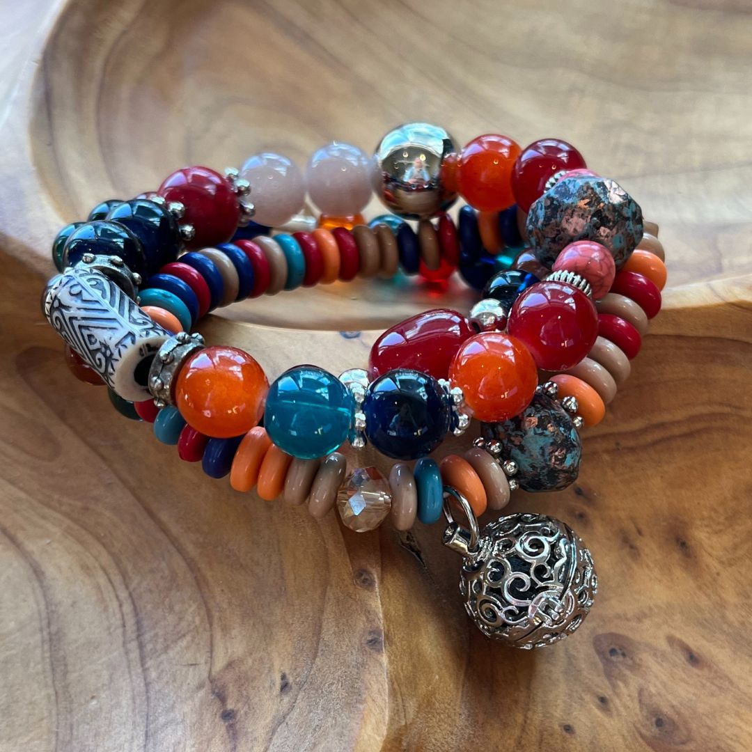 Trio of stretchy beaded bracelets with various shaped beads in reds, oranges, turquoise and more. A silver ball pendant contains a lava rock for essential oils.