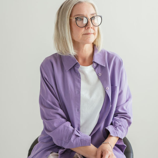 Woman with light hair wearing purple button down shirt and black framed glasses