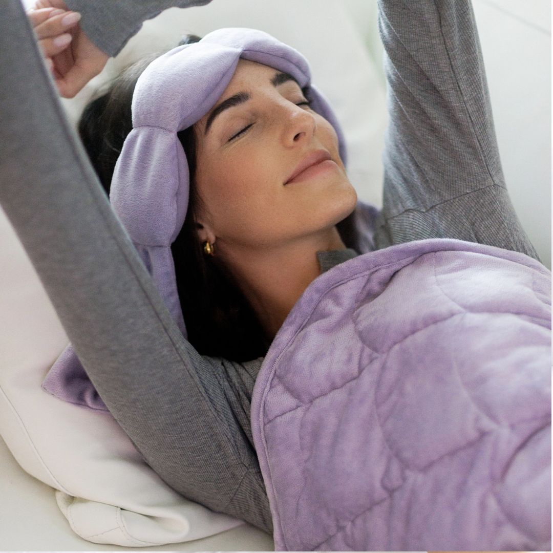 Woman laying in bed with wisteria colored Nodpod weighted eye pillow and blanket
