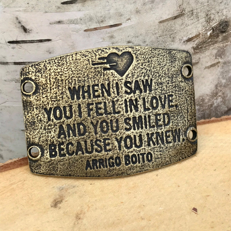 Antique brass finish Lenny & Eva bracelet sentiment that reads, "When I saw you I fell in love, and you smiled because you knew." Quote by Arrigo Boito. A heart etching is above the quote.
