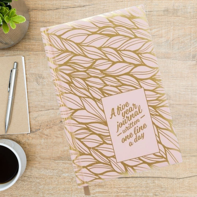 Journal with a pink and gold leaf design on the cover and in the corner "A five year journal written one line a day" is written in gold