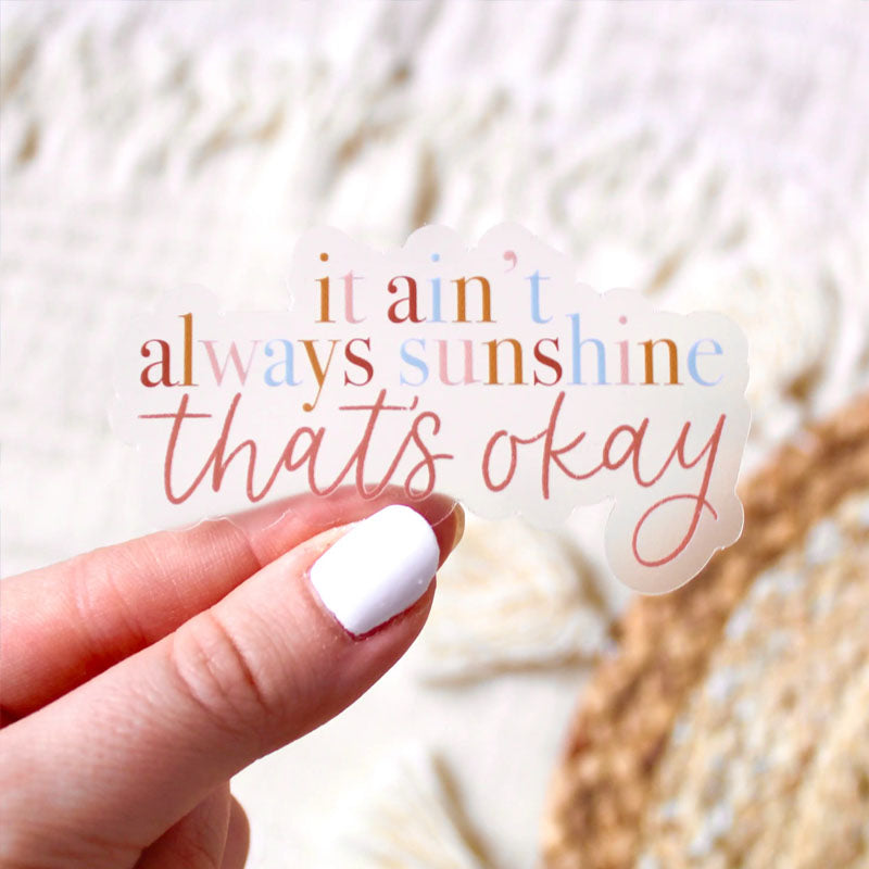 Sticker with clear background that says "it ain't always sunshine that's ok" written in earthy pastel colors