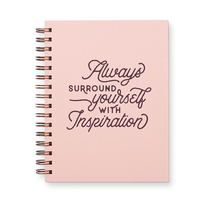 Dusty pink colored journal with "Always surround yourself with inspiration" written in dark pink on the cover. There is a spiral binding.
