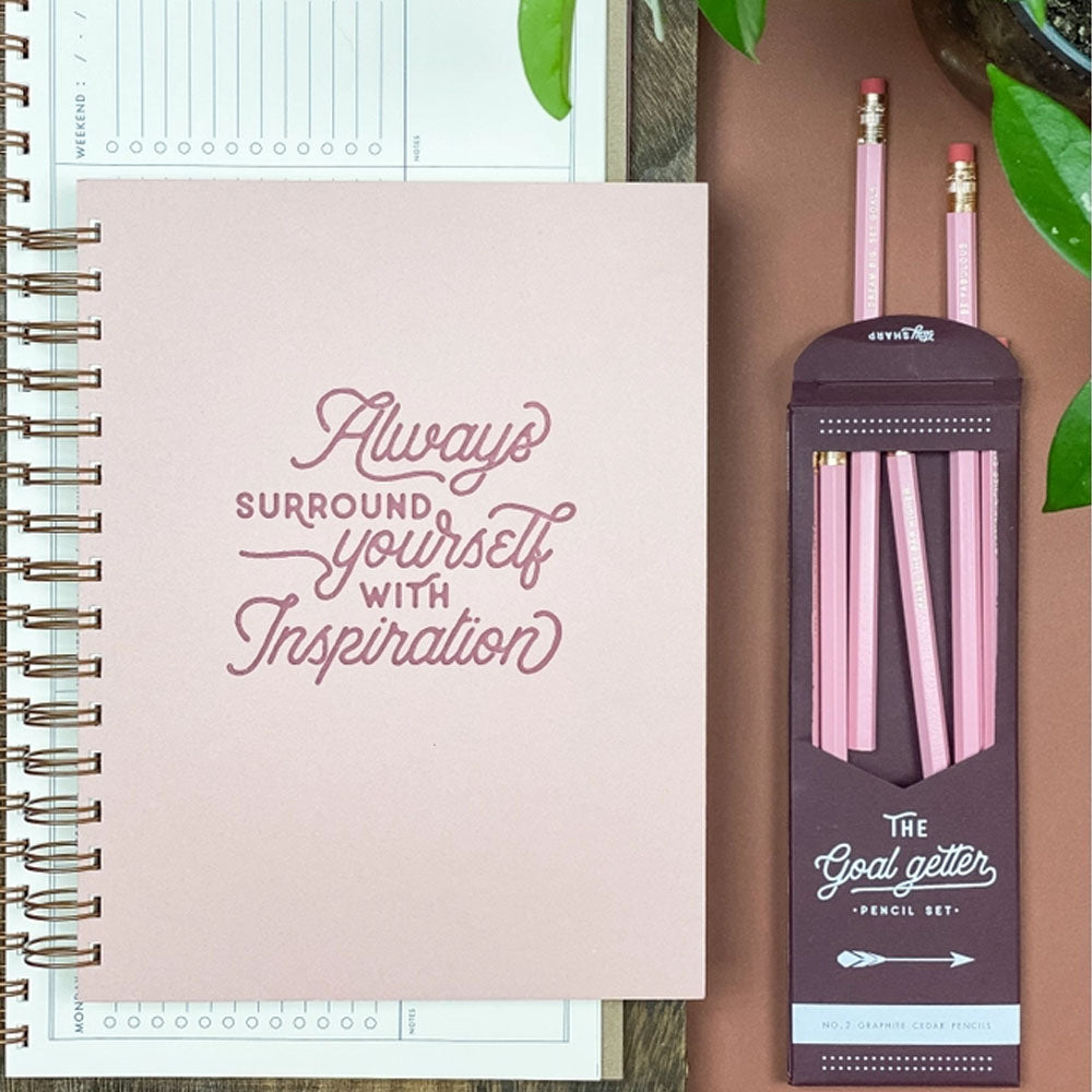 The journal on a desk with pink pencils and a planner sitting underneath