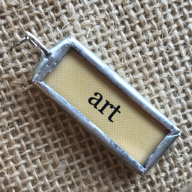 Necklace pendant with a yellow background and the word "art"