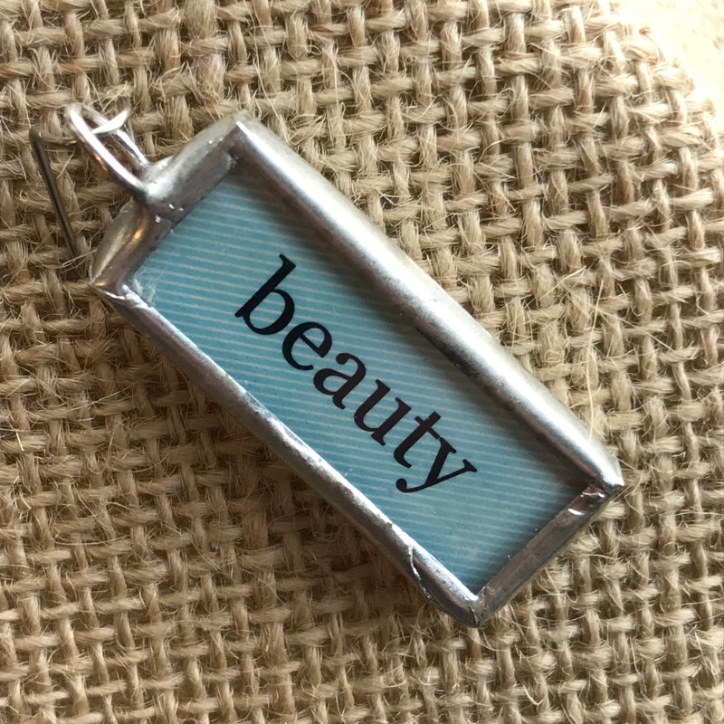 Soldered pendant with a blue background and the word "beauty"