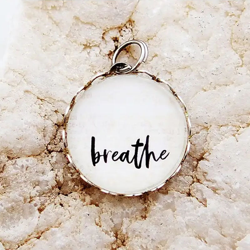 Round necklace pendant with the word "breathe" on a white background.