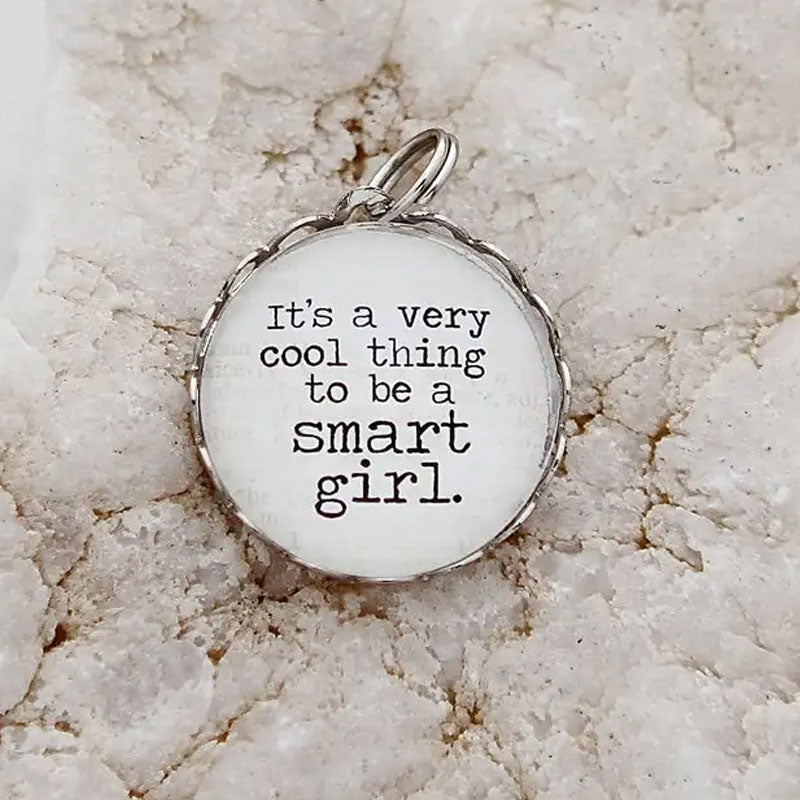 Round necklace pendant with silver metal edge. White background with black text that reads "It's a very cool thing to be a smart girl."