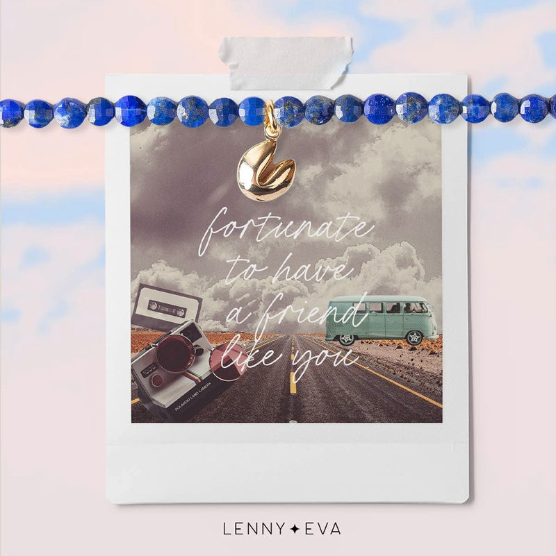 Dark blue lapis lazuli beaded bracelet with tiny gold fortune cookie charm. On a card with a road-trip photo background that reads "fortunate to have a friend like you"