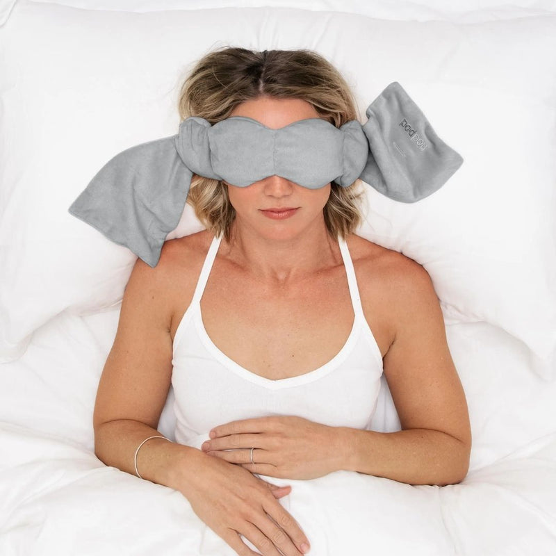 Woman laying in bed with gray eye pillow over eyes