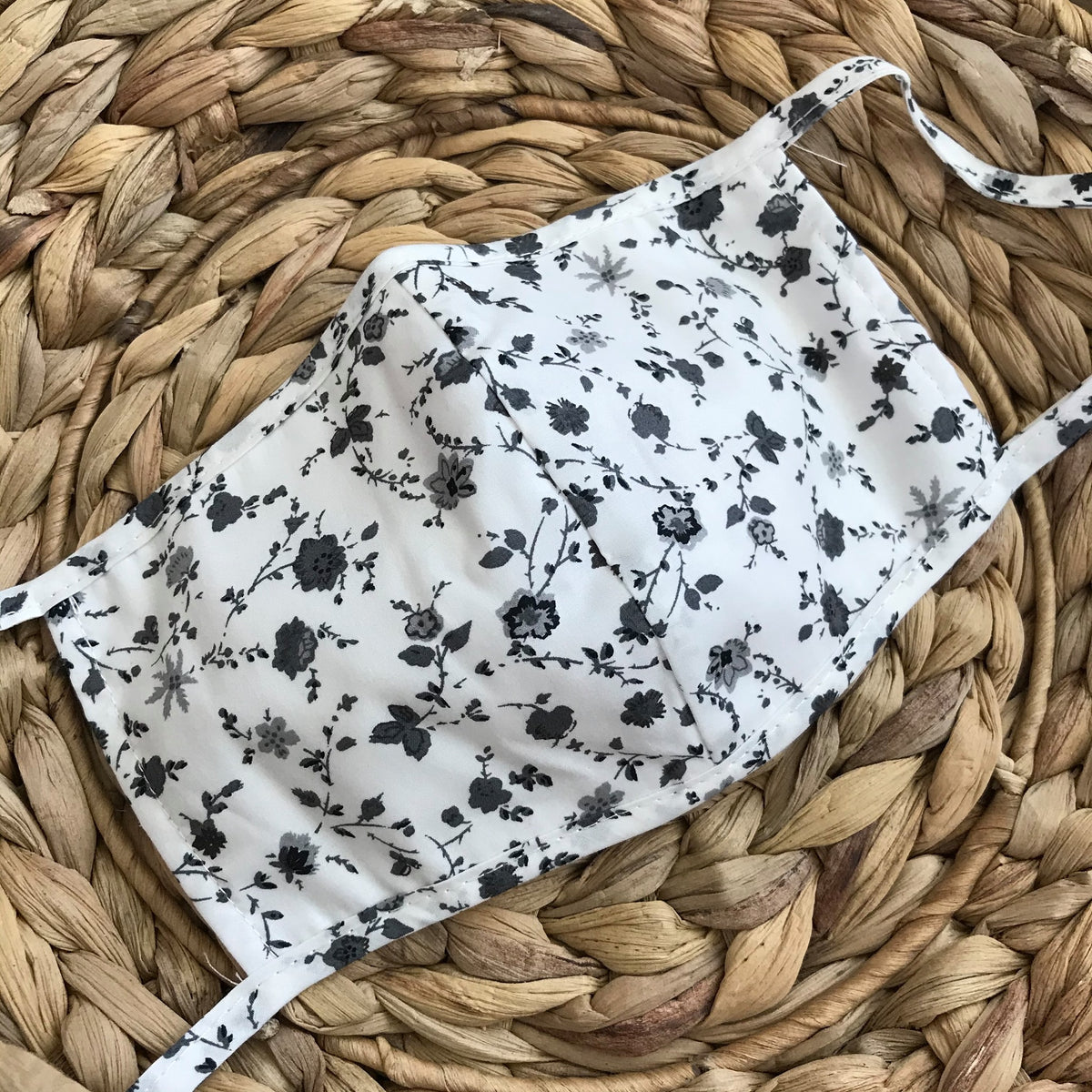 Slightly off white and gray floral printed face mask with tie straps to tie in the back of your head.