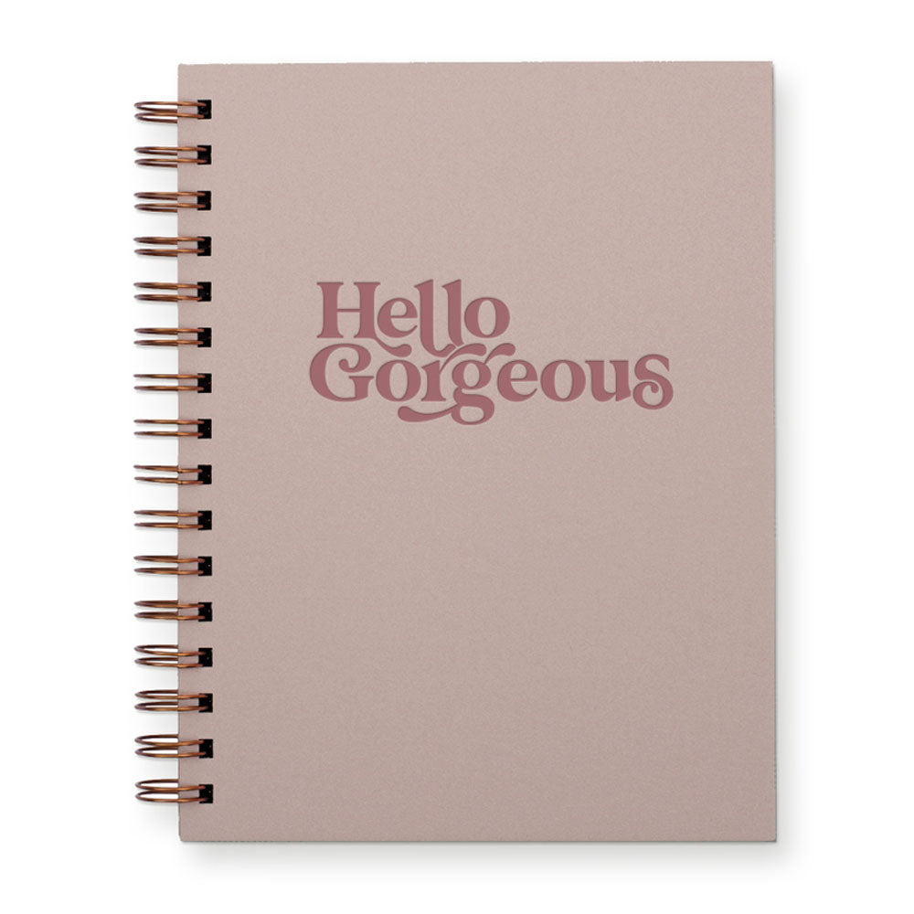 Dusty rose colored journal with "Hello Gorgeous" written on the cover in dark rose color. There is a spiral binding on the side.