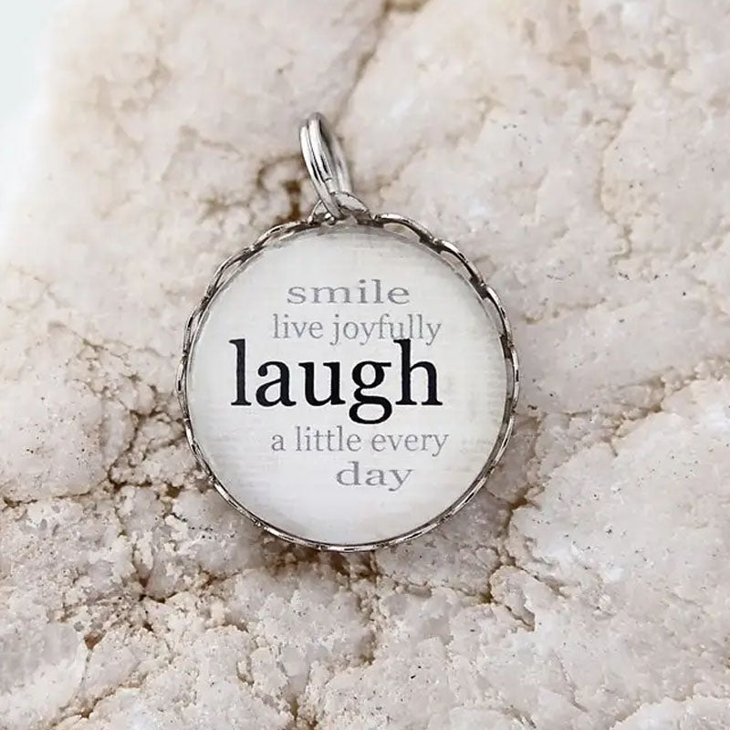 Round necklace pendant with a white background and silver metal edge. Text on pendant reads "smile live joyfully laugh a little every day"