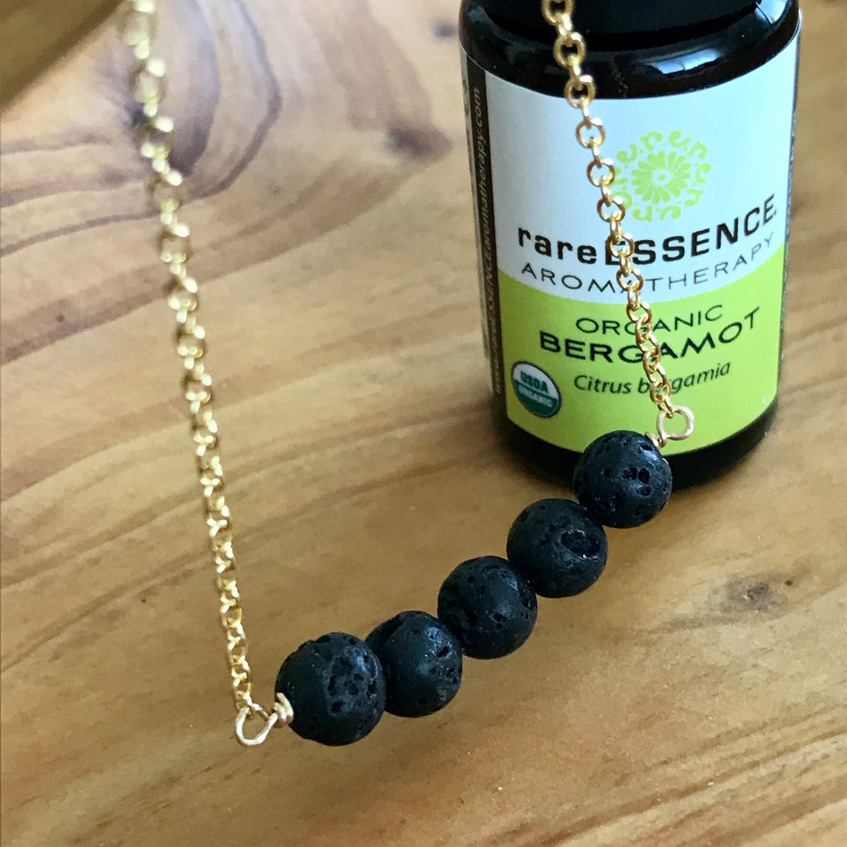 Gold Necklace with Black Lava Rocks for Essential Oil Aromatherapy. Pictured with Organic Bergamot Essential Oil by rareESSENCE.