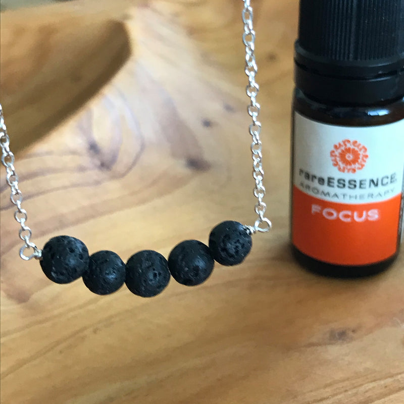 Sterling silver necklace with a band of black lava rocks to diffuse your favorite essential oils. Pictured with Focus essential oil by rareESSENCE. Made in the U.S.A. by Lotus Jewelry Studio.