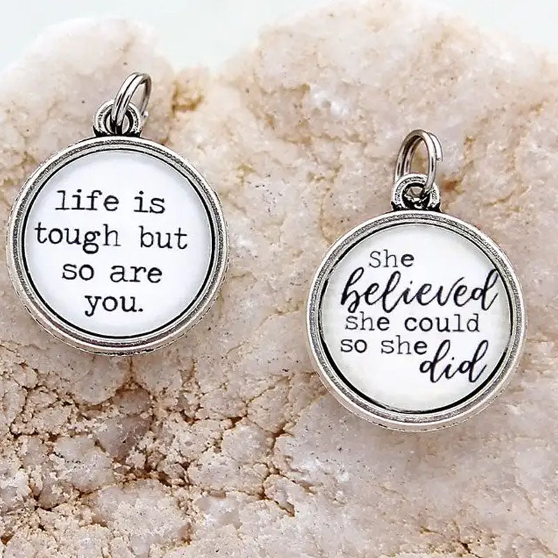 Necklace pendant with the text "life is tough but so are you" on one side and "she believed she could so she did" on the reverse