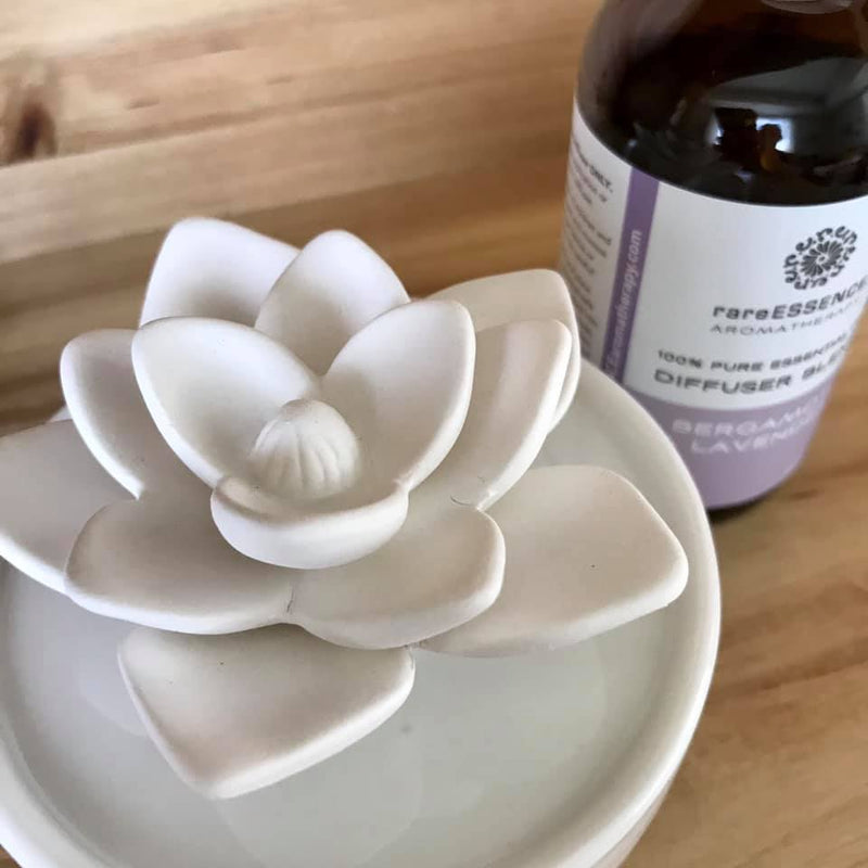Ivory colored ceramic lotus flower diffuser with bottle of bergamot and lavender essential oil.