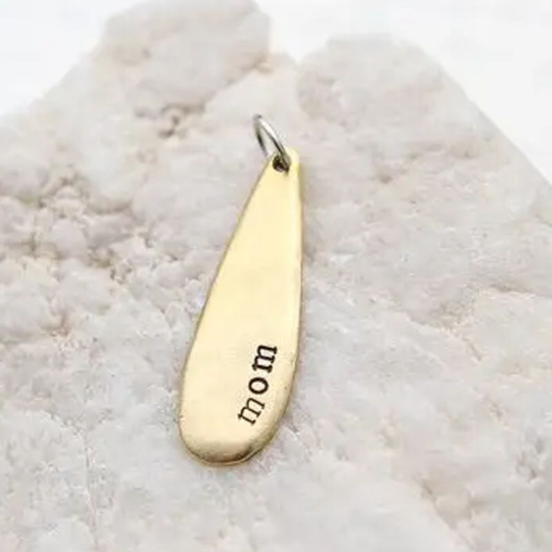 Gold teardrop necklace pendant stamped with the word "mom"