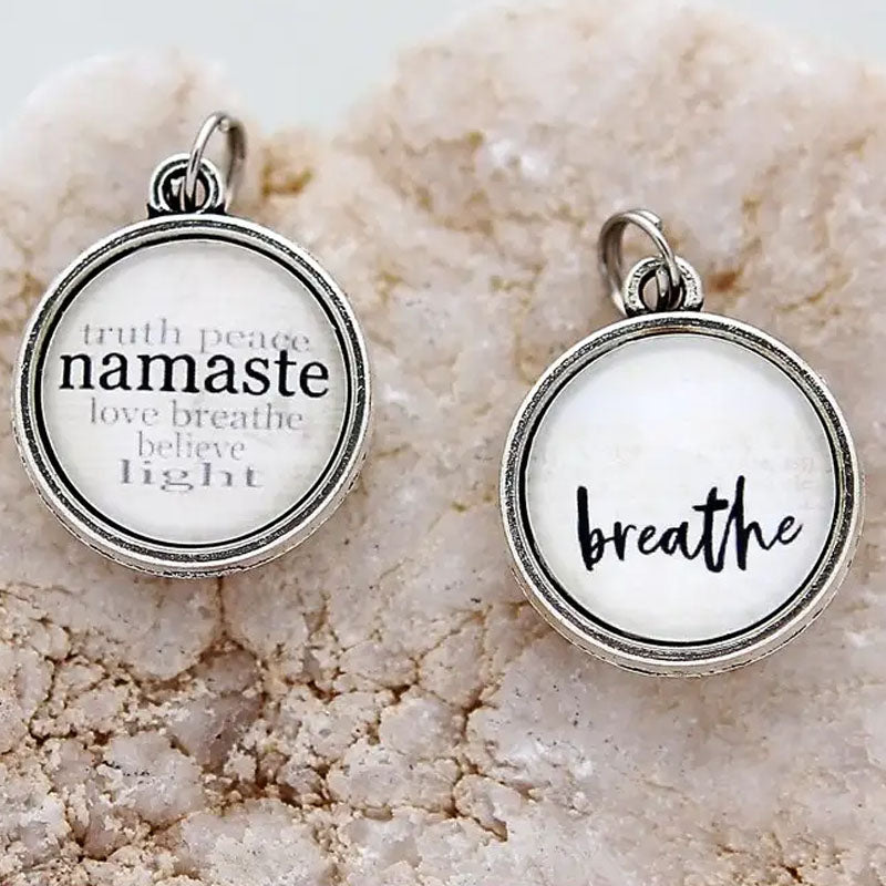 Necklace pendant that says "breathe" on one side and the reverse says "truth peace namaste love breathe believe light"