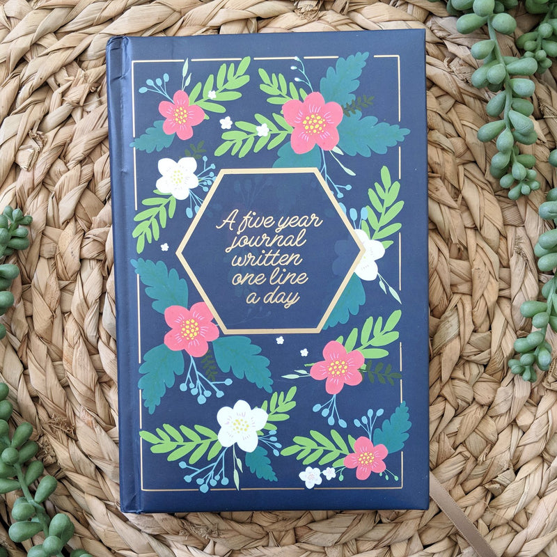 Navy blue journal with pink and ivory flowers on the cover. Title written in gold is "A five year journal written one line a day"