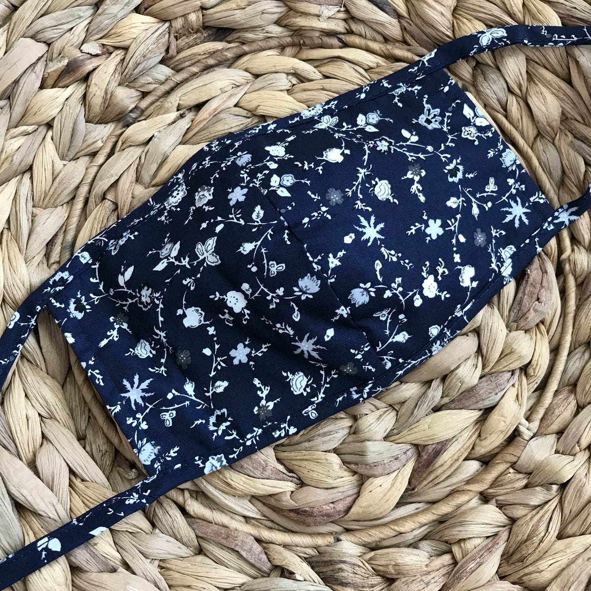 Navy blue face mask with a gray and white floral print. Mask has long ties to tie in the back of the head.