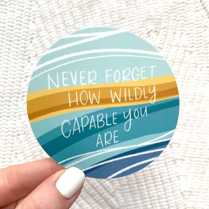 3" circle sticker with a blue wavy background with "Never forget how wildly capable you are" printed in white.