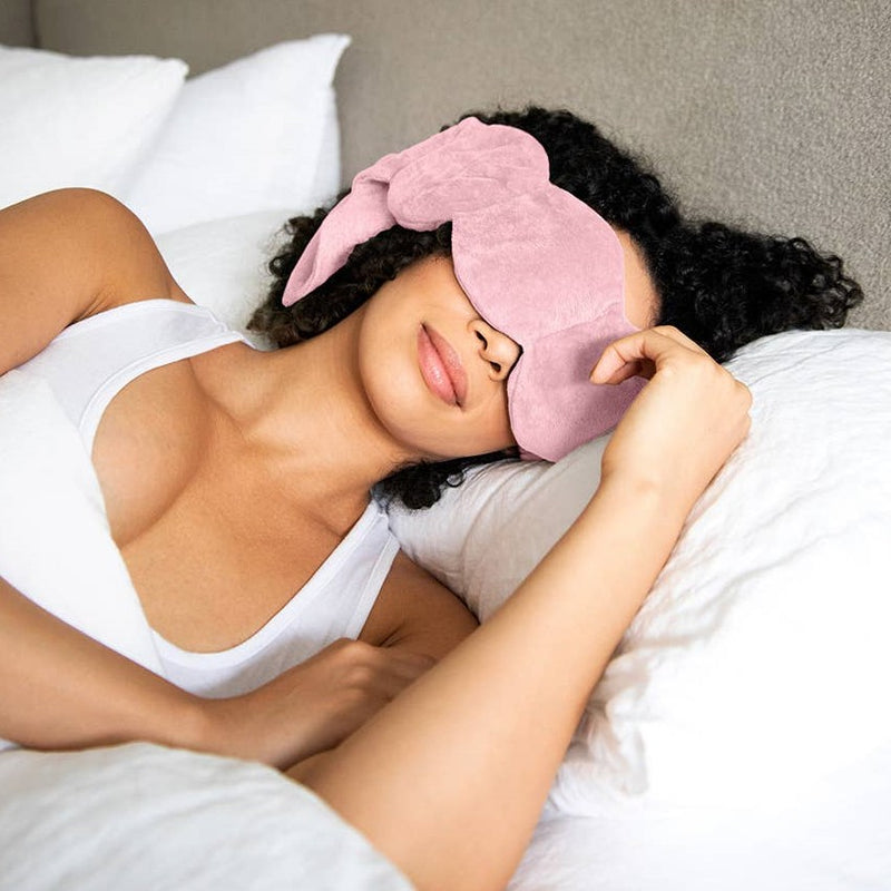 Woman laying on her side in bed with pink eye mask over her eyes