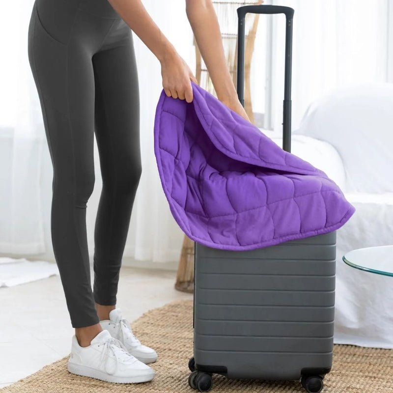 Travel size purple weighted blanket sitting on a gray suitcase