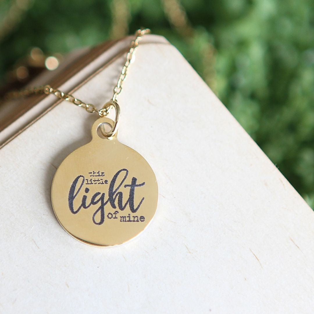 Round gold pendant engraved with "this little light of mine" on a gold necklace chain