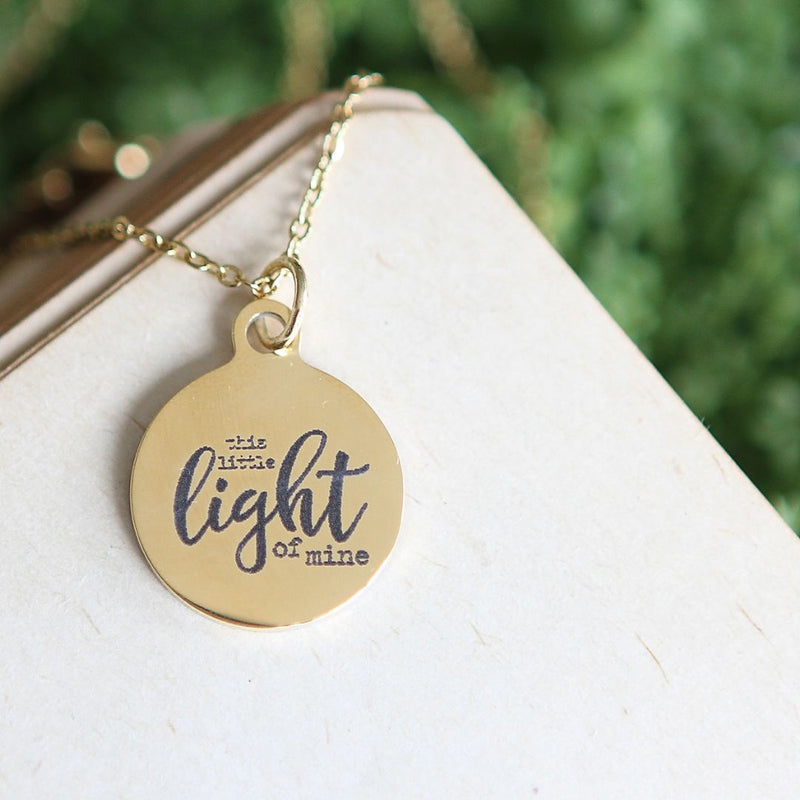 Round gold pendant engraved with "this little light of mine" on a gold necklace chain