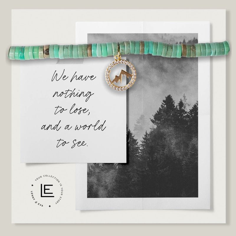 Green beaded bracelet with gold and cubic zirconia mountain charm on a card that reads, "We have nothing to lose, and a world to see."