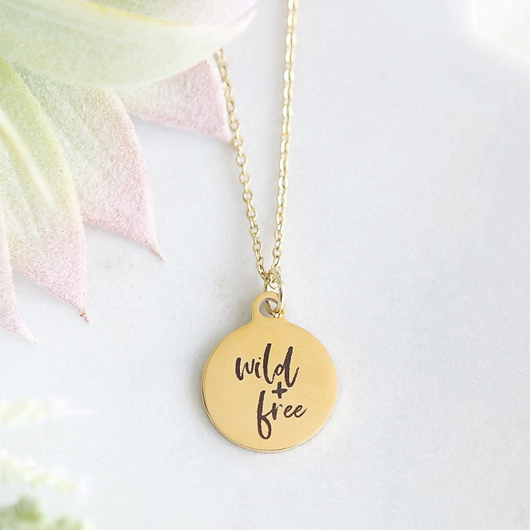 Round gold pendant engraved with "wild + free" on a gold necklace chain