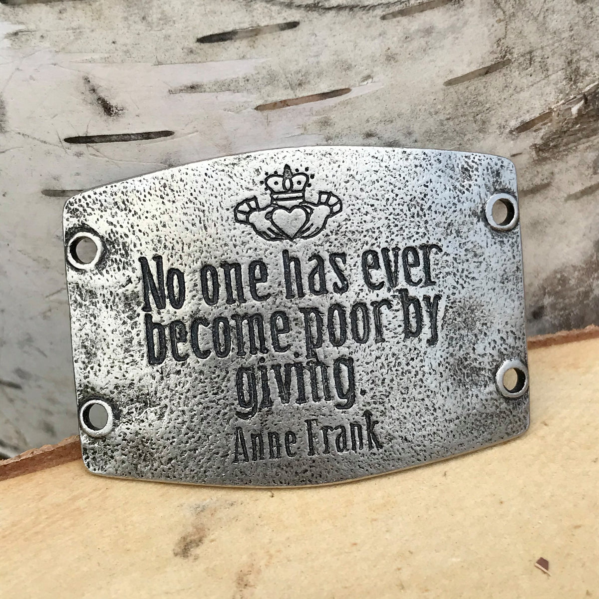 Antique silver finish Lenny & Eva bracelet sentiment that reads, "No one has ever become poor by giving." Quote by Anne Frank. Design above quote is hands holding a heart and crown.