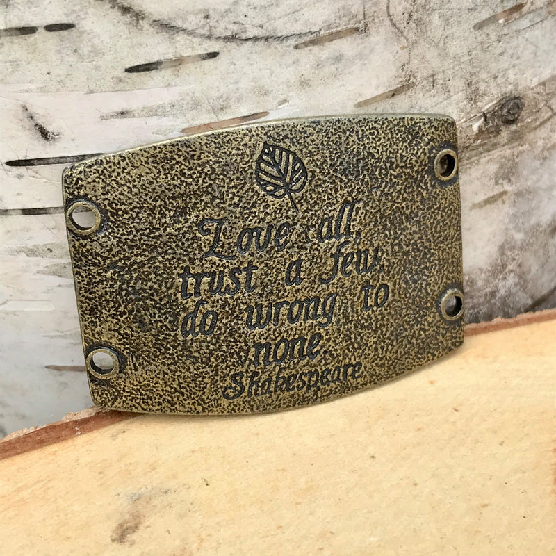 Antique brass finish Lenny & Eva bracelet sentiment that reads, "Love all, trust a few, do wrong to none." Quote by Shakespeare. Design of leaf above the quote.
