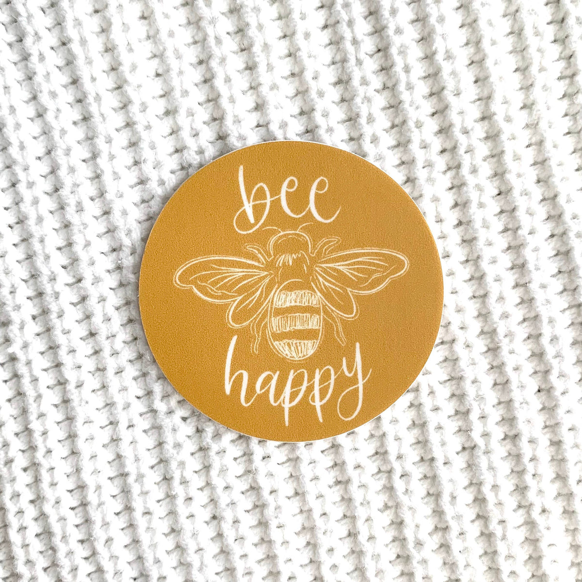 Round mustard yellow sticker with a picture of a bee that says "bee happy"