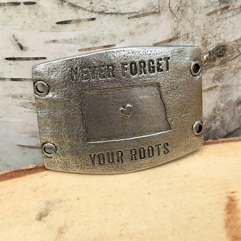 Antique silver finish Lenny & Eva bracelet sentiment that reads, "Never forget your roots" Design features a heart inside an outline of the state of North Dakota.