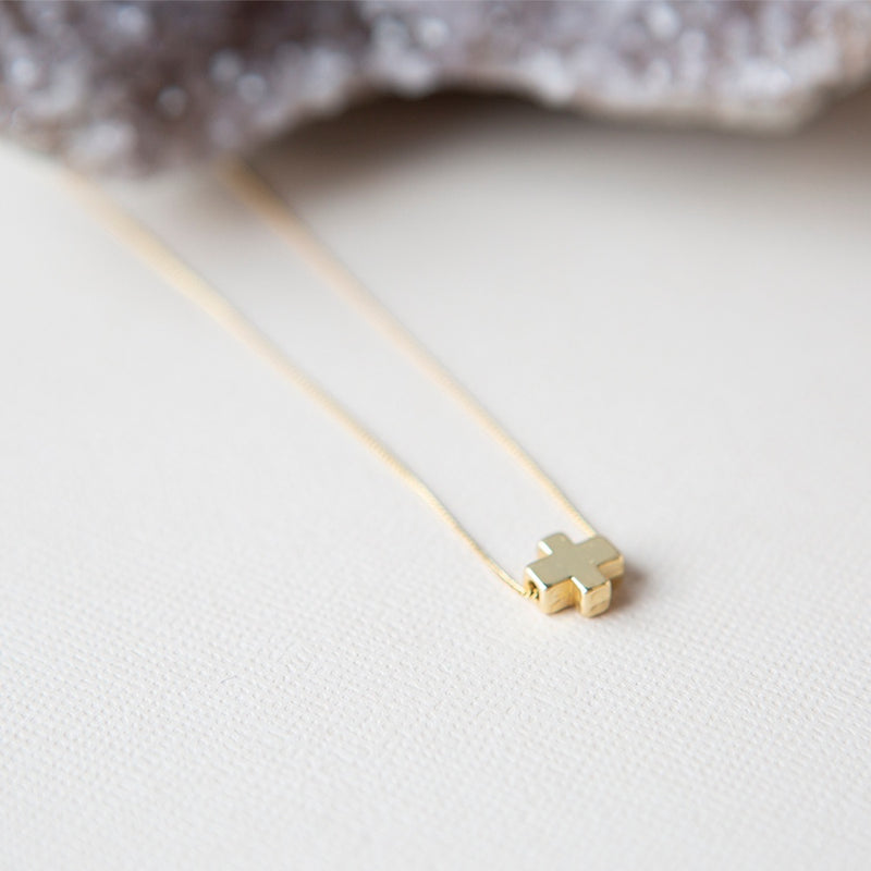 A small gold cross charm on a thin gold necklace