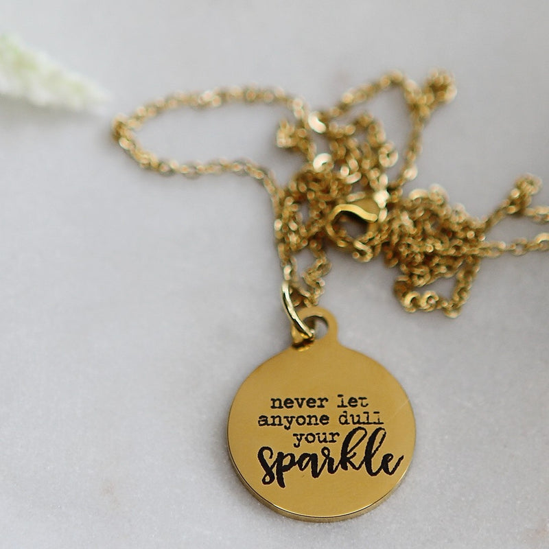 Round gold pendant engraved with "never let anyone dull your sparkle"
