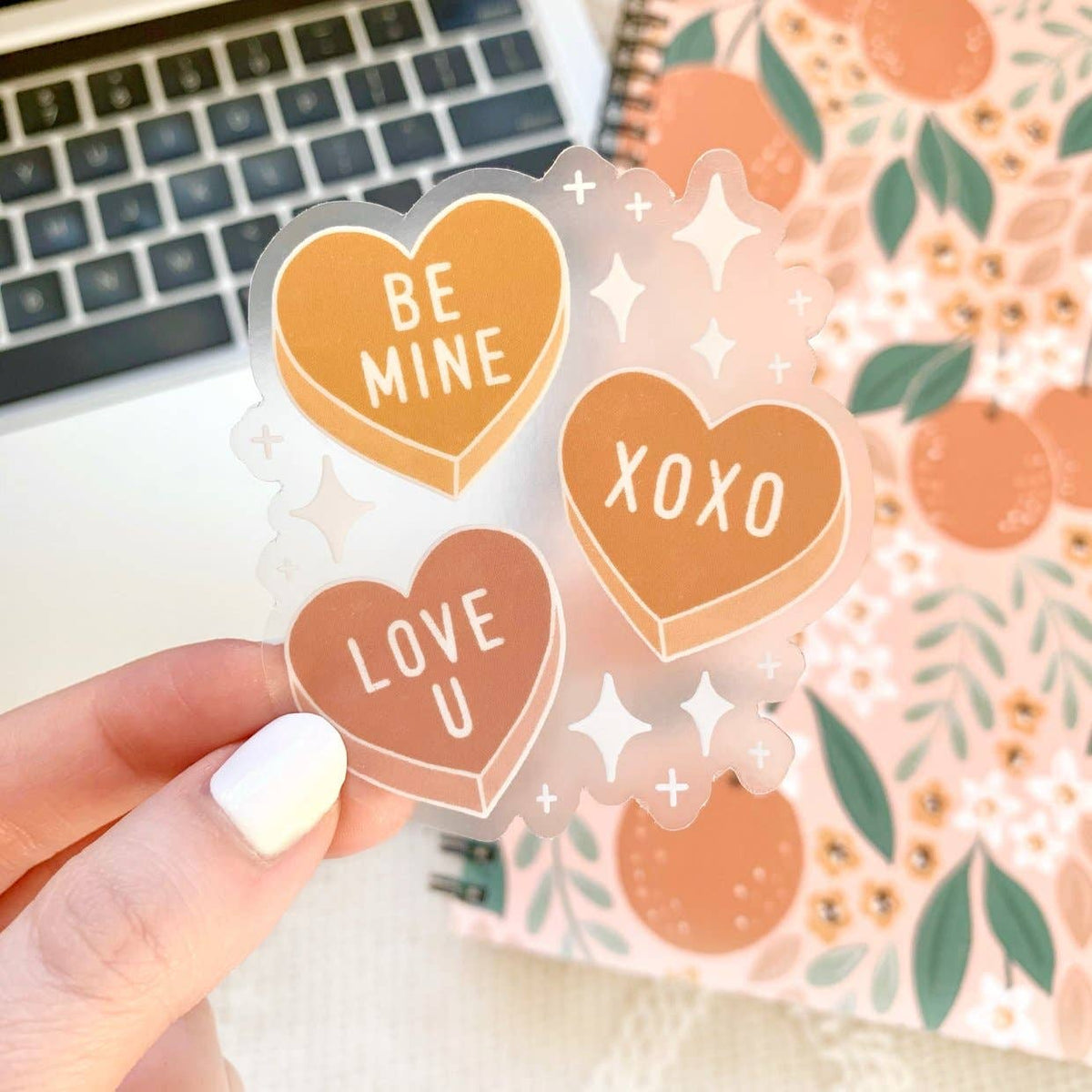 Clear sticker with rust and rose colored valentine's candy hearts and white diamonds. Hearts say "Be Mine", "Love U", and "XOXO"